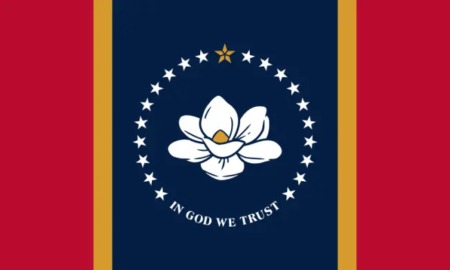 The official flag of the state of Mississippi. It has red, yellow, and blue stripes. In the middle is a white magnolia flower with stars in a circle around it. At the bottom, the words 'In God We Trust'